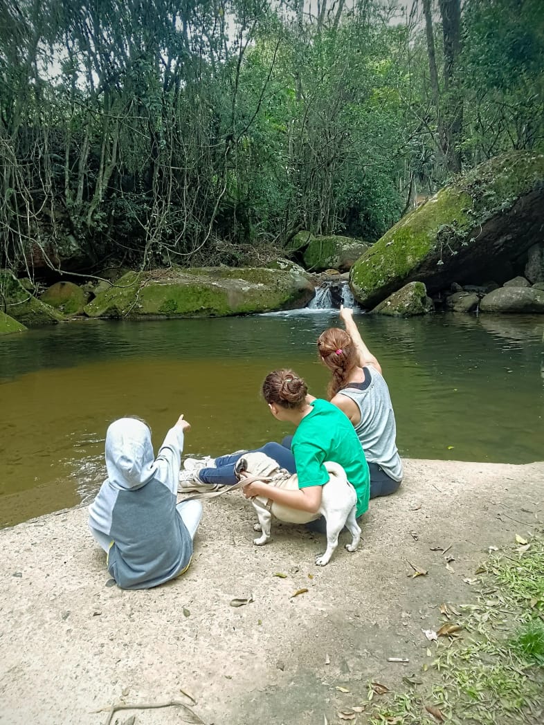 Família sentada na pedra, com um cachorro, na beira da piscina natural da cachoeira